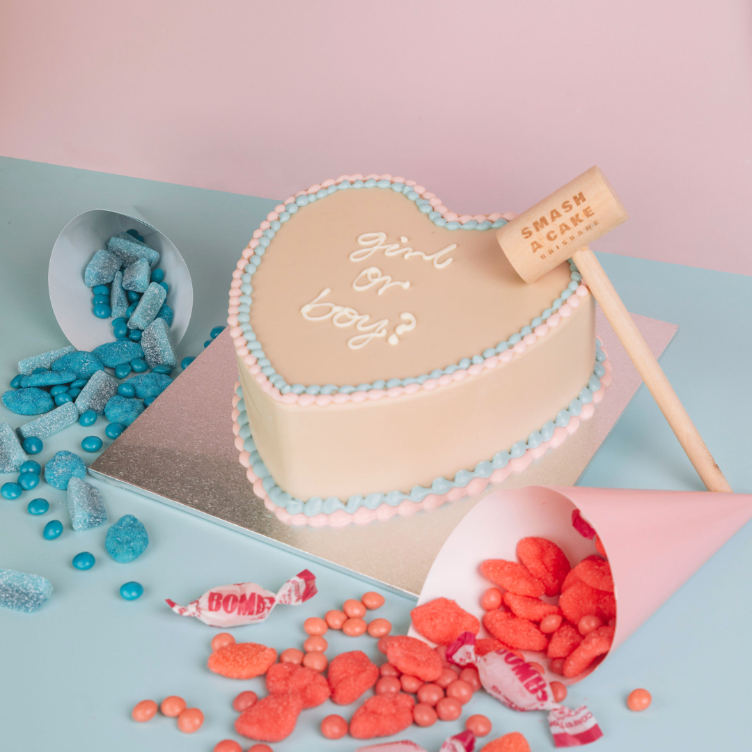 Gender reveal chocolate heart smash cake with blue or pink confectionery.